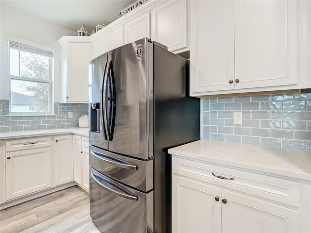 kitchen with light hardwood / wood-style flooring, white cabinetry, stainless steel fridge with ice dispenser, light stone countertops, and decorative backsplash