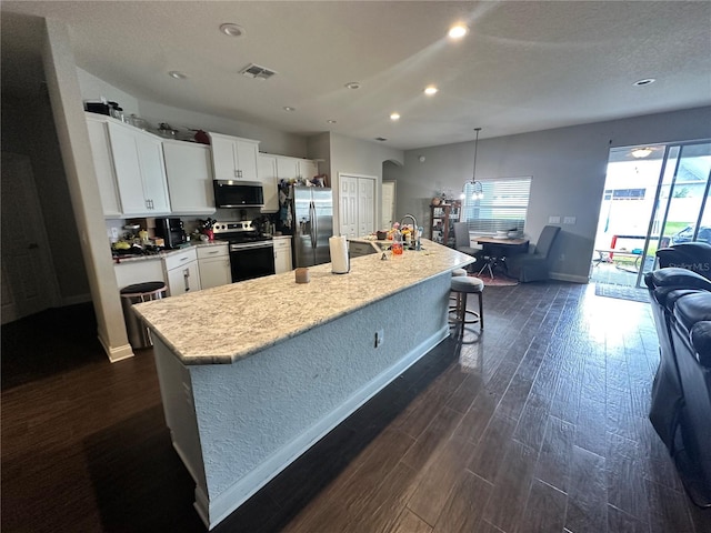 kitchen with decorative light fixtures, white cabinets, a kitchen island with sink, and appliances with stainless steel finishes