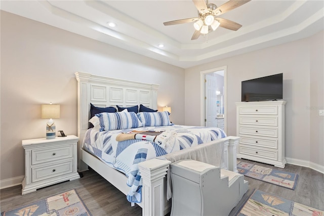 bedroom with a tray ceiling, dark wood-type flooring, ensuite bath, and ceiling fan