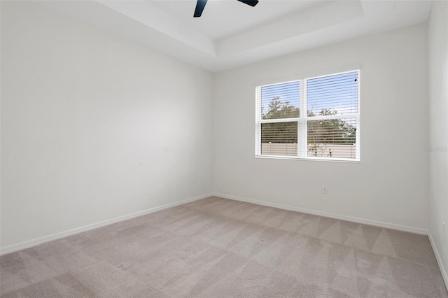 empty room featuring light colored carpet, ceiling fan, and a raised ceiling