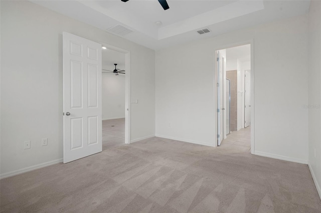 unfurnished bedroom featuring ceiling fan, a tray ceiling, and light carpet