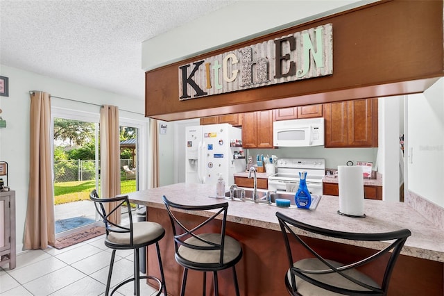 kitchen featuring a breakfast bar, light tile patterned floors, brown cabinetry, a textured ceiling, and white appliances