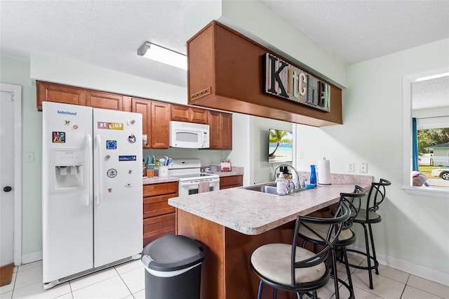 kitchen featuring white appliances, brown cabinets, a peninsula, a textured ceiling, and a sink