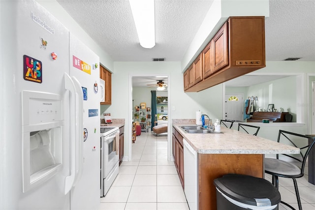 kitchen featuring white appliances, a sink, visible vents, brown cabinets, and a kitchen bar