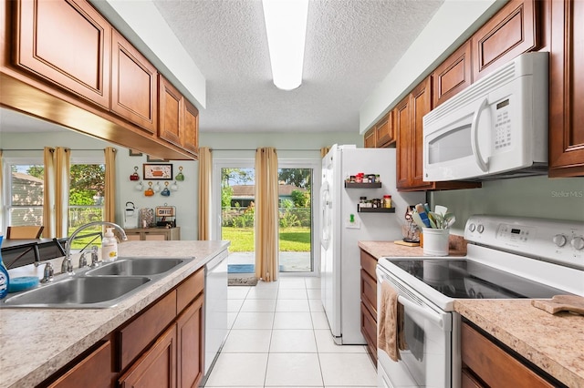 kitchen featuring brown cabinetry, white appliances, a sink, and light tile patterned floors