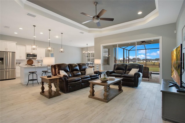 living room featuring crown molding, a tray ceiling, ceiling fan with notable chandelier, and light hardwood / wood-style floors