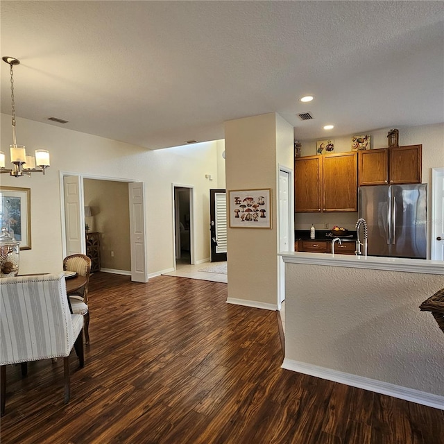 kitchen with dark wood finished floors, brown cabinets, decorative light fixtures, freestanding refrigerator, and an inviting chandelier