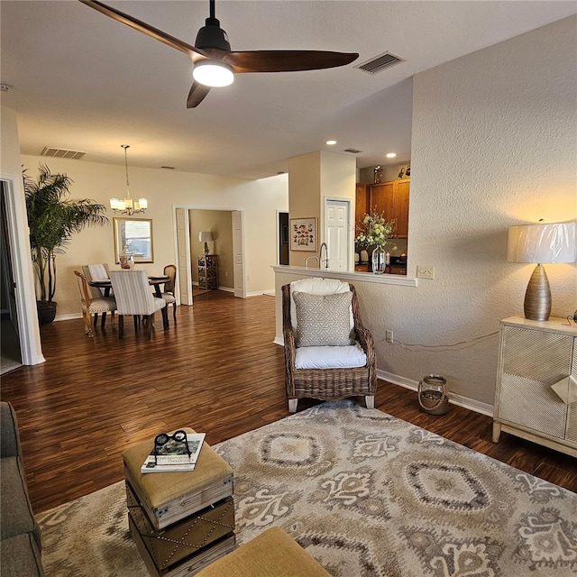 living area with baseboards, visible vents, wood finished floors, and ceiling fan with notable chandelier