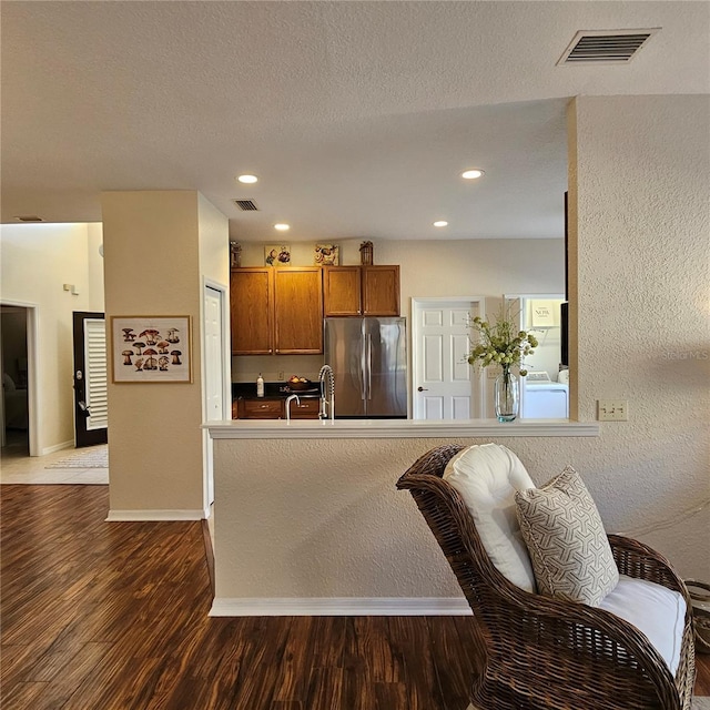 kitchen featuring baseboards, visible vents, dark wood finished floors, brown cabinets, and freestanding refrigerator