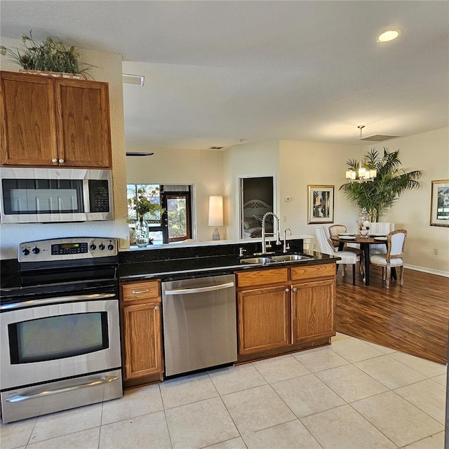 kitchen featuring light tile patterned floors, dark countertops, appliances with stainless steel finishes, brown cabinetry, and a sink