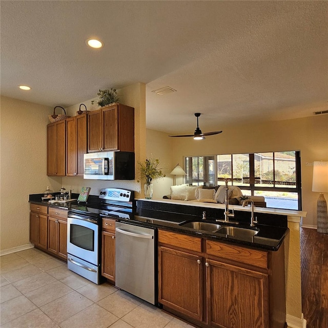 kitchen with dark countertops, appliances with stainless steel finishes, open floor plan, and a sink