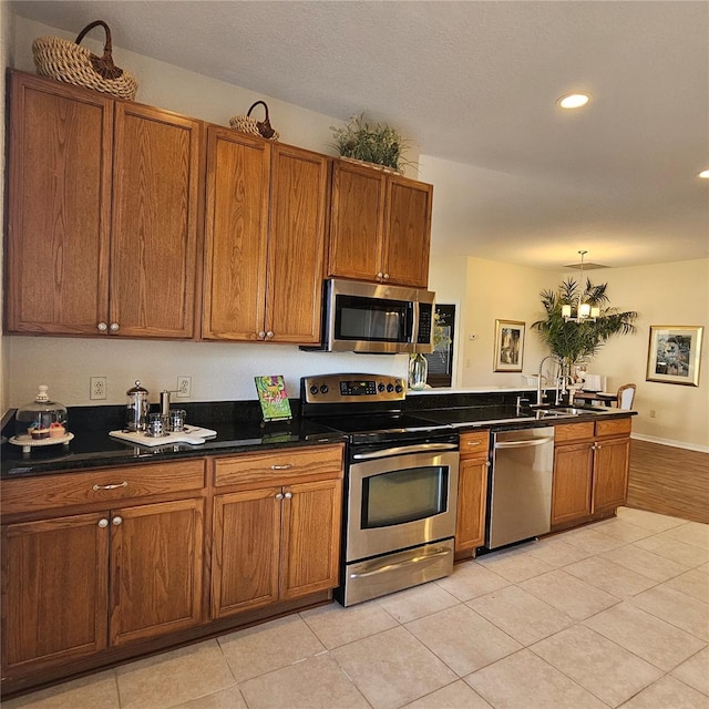 kitchen featuring stainless steel appliances, brown cabinetry, dark countertops, and a sink