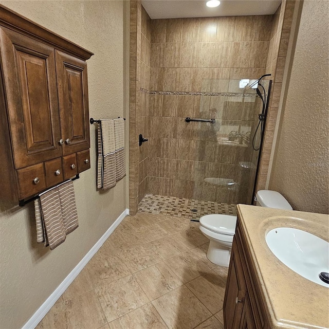 bathroom with a textured wall, toilet, vanity, a walk in shower, and baseboards