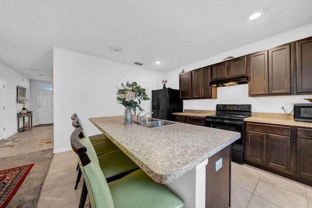 kitchen featuring a kitchen breakfast bar, sink, light tile patterned flooring, an island with sink, and black appliances