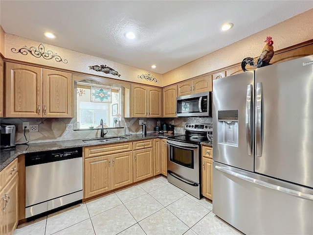 kitchen with sink, tasteful backsplash, light tile patterned floors, appliances with stainless steel finishes, and dark stone counters