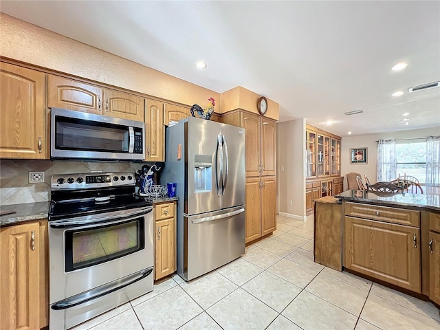 kitchen featuring light tile patterned flooring, appliances with stainless steel finishes, dark stone countertops, and decorative backsplash