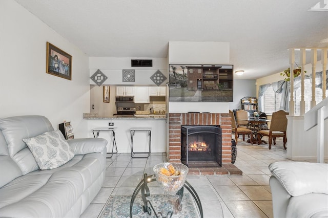 living room with a textured ceiling, a brick fireplace, and light tile patterned floors