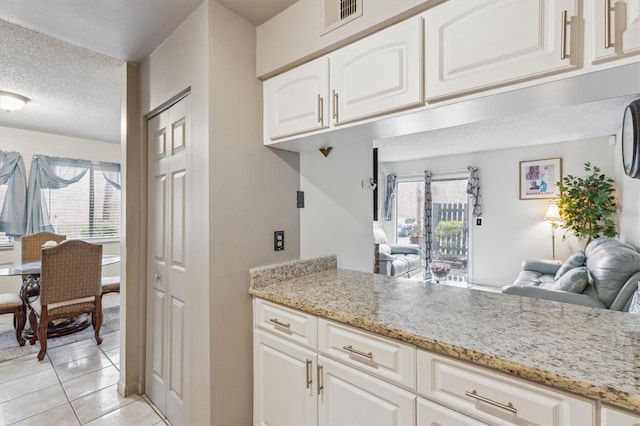 kitchen with white cabinetry, light tile patterned floors, light stone countertops, and a textured ceiling