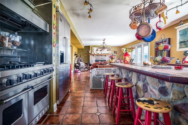 kitchen with a kitchen breakfast bar, dark tile patterned floors, high quality appliances, backsplash, and a stone fireplace