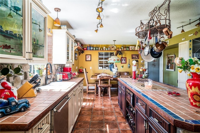 kitchen featuring sink, dark brown cabinetry, dishwasher, and tile counters