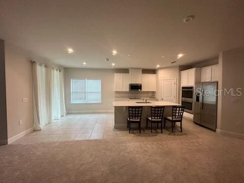 kitchen featuring an island with sink, white cabinetry, light tile patterned floors, a breakfast bar, and stainless steel appliances