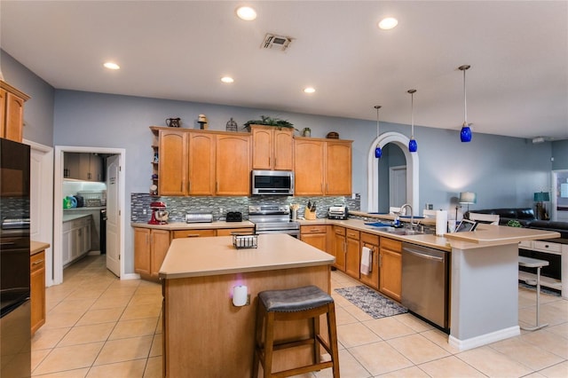 kitchen with a kitchen island with sink, hanging light fixtures, a breakfast bar area, and stainless steel appliances