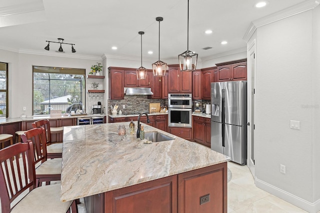 kitchen with sink, appliances with stainless steel finishes, light stone counters, a center island with sink, and decorative backsplash