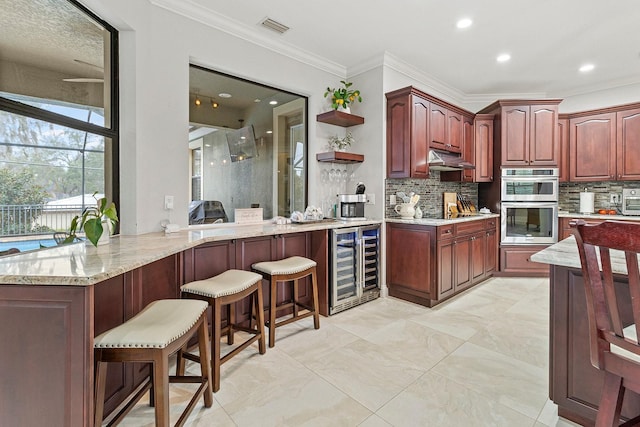 kitchen featuring tasteful backsplash, a kitchen breakfast bar, kitchen peninsula, double oven, and beverage cooler