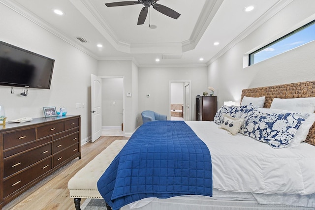 bedroom featuring ceiling fan, ensuite bathroom, ornamental molding, a raised ceiling, and light wood-type flooring