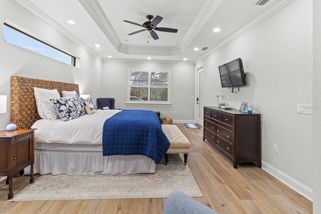 bedroom featuring multiple windows, crown molding, light hardwood / wood-style flooring, and a tray ceiling