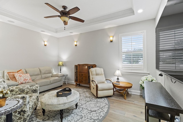 living room featuring a raised ceiling, ornamental molding, ceiling fan, and light wood-type flooring