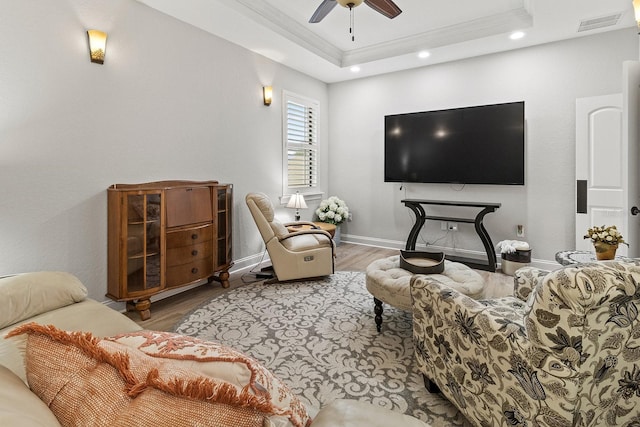 living room with a raised ceiling, crown molding, wood-type flooring, and ceiling fan