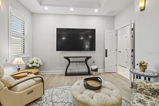 living room with crown molding, a tray ceiling, and light wood-type flooring