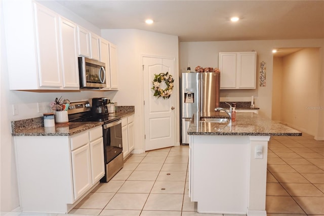 kitchen featuring appliances with stainless steel finishes, white cabinetry, dark stone countertops, light tile patterned floors, and a center island with sink