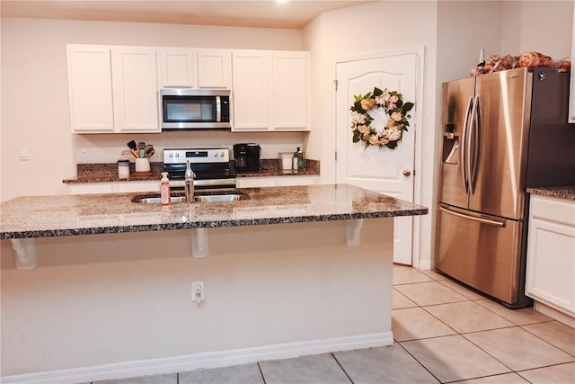 kitchen featuring white cabinetry, appliances with stainless steel finishes, an island with sink, and dark stone countertops