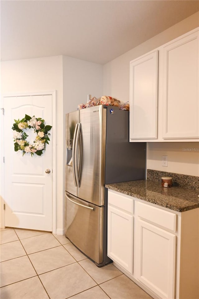 kitchen with stainless steel refrigerator with ice dispenser, dark stone counters, light tile patterned floors, and white cabinets