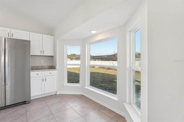 kitchen featuring stainless steel refrigerator, light tile patterned floors, vaulted ceiling, and white cabinets