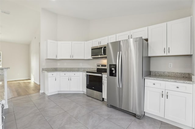 kitchen featuring white cabinetry, light stone countertops, stainless steel appliances, and light tile patterned flooring