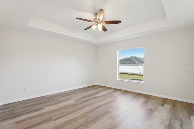 spare room with ceiling fan, a tray ceiling, and light hardwood / wood-style flooring