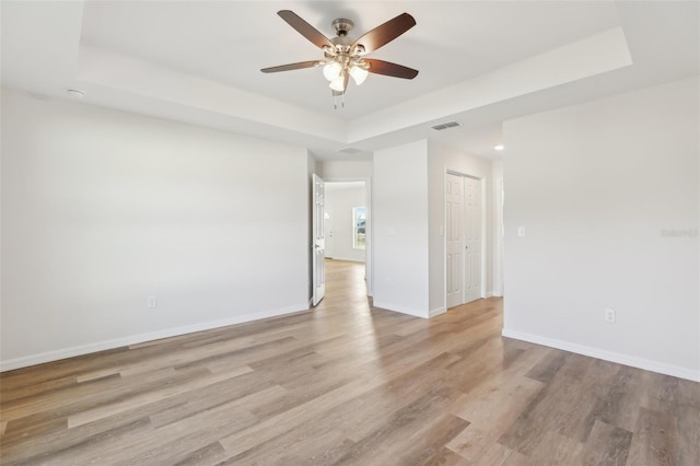 empty room featuring ceiling fan, a tray ceiling, and light wood-type flooring