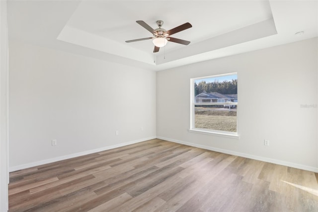 unfurnished room with a raised ceiling, wood-type flooring, and ceiling fan