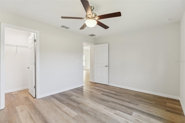 unfurnished bedroom with a walk in closet, a closet, ceiling fan, and light wood-type flooring