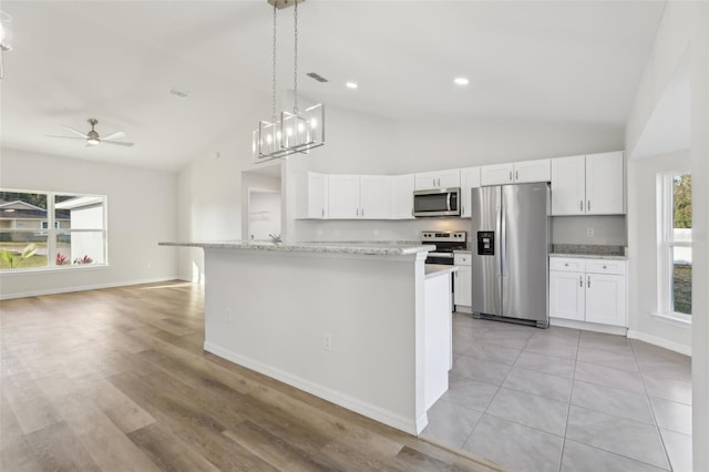 kitchen featuring pendant lighting, appliances with stainless steel finishes, white cabinetry, light stone countertops, and a center island with sink