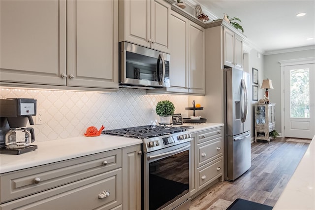 kitchen featuring tasteful backsplash, light hardwood / wood-style flooring, ornamental molding, gray cabinets, and stainless steel appliances