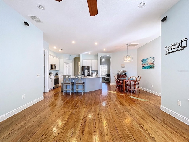 kitchen featuring hardwood / wood-style floors, decorative light fixtures, white cabinetry, a kitchen island with sink, and stainless steel appliances