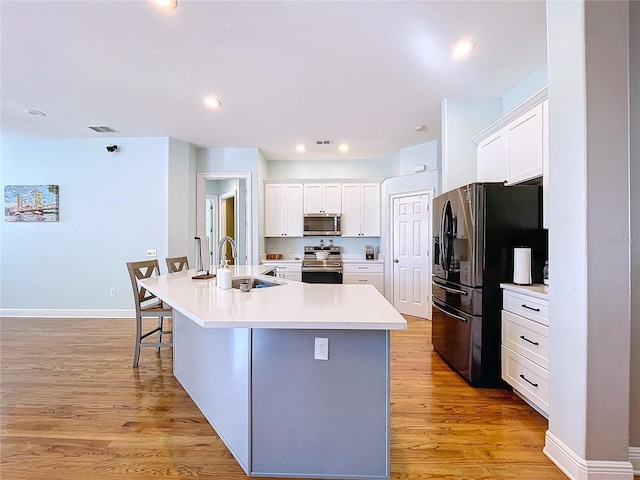 kitchen with stainless steel appliances, a kitchen island with sink, sink, and white cabinets