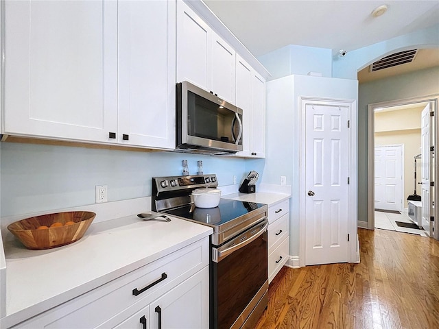 kitchen with stainless steel appliances, hardwood / wood-style floors, and white cabinets