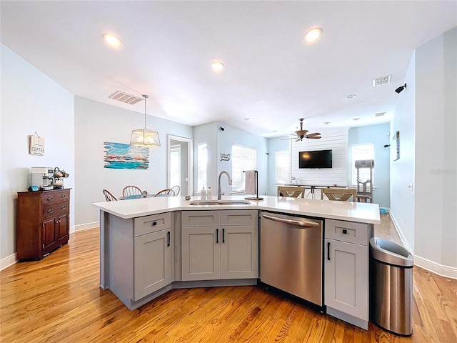 kitchen featuring sink, hanging light fixtures, stainless steel dishwasher, gray cabinets, and a kitchen island with sink