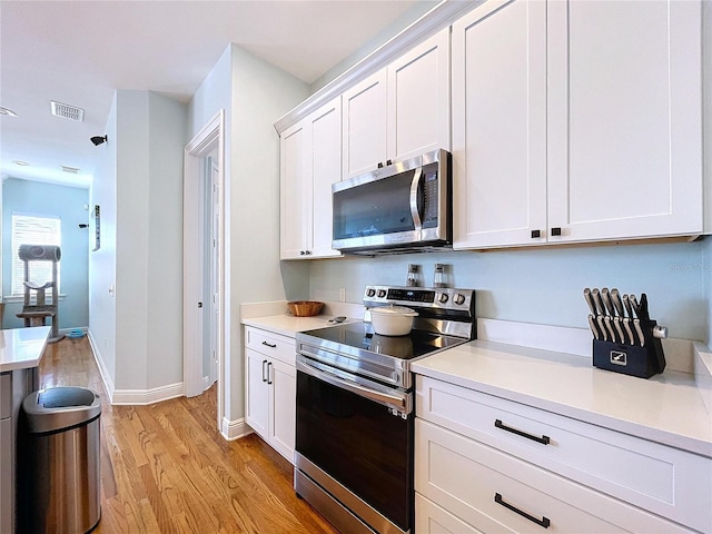 kitchen with light hardwood / wood-style flooring, stainless steel appliances, and white cabinets