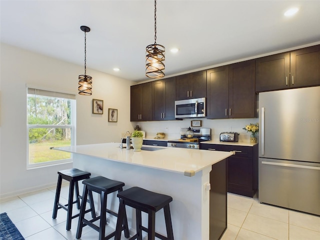 kitchen with sink, decorative light fixtures, dark brown cabinets, stainless steel appliances, and a kitchen island with sink